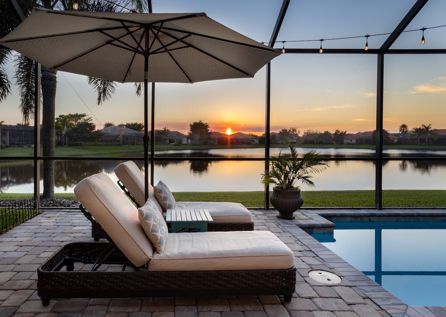 Florida screened swimming pool with lounge chairs overlooking lake at sunset