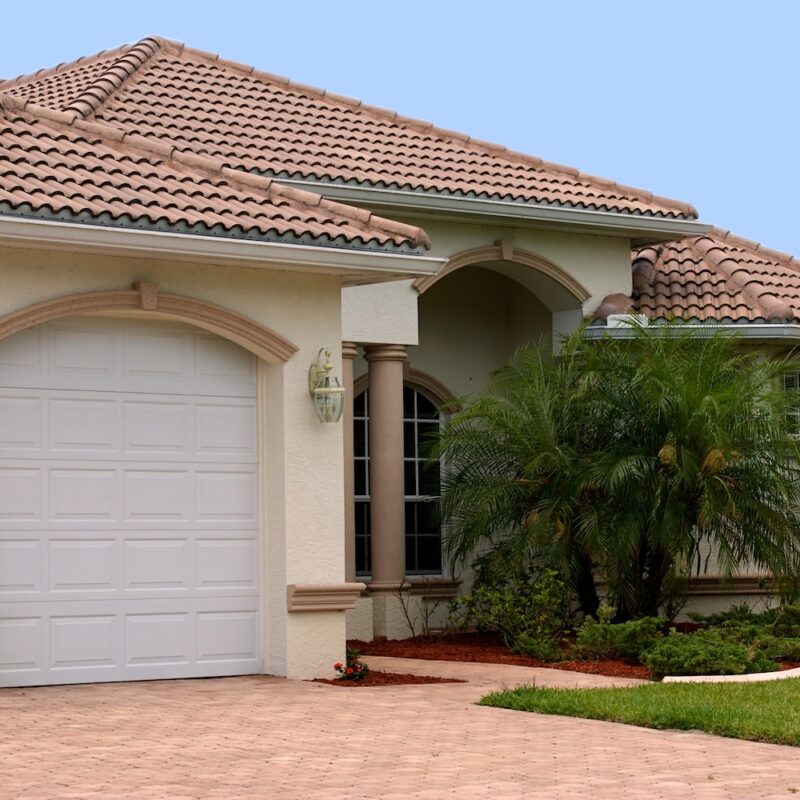 a generic one story florida home with garage, palm trees and a clear blue sky
